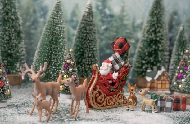 Christmas scene featuring Santa Claus in a sleigh with reindeer surrounded by trees.