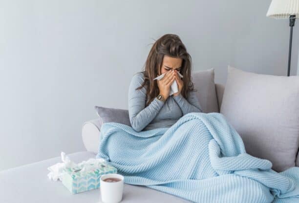 A woman sitting on a couch with a cozy blanket and a cup of coffee dispelling flu myths.